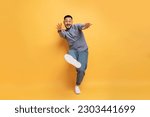 Cheerful young asian man having fun on yellow studio background, happy positive millennial guy reaching hands and showing shoe sole at camera, having fun, full length shot, copy space