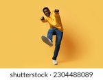 Small photo of Happy handsome curly young black man in stylish casual outfit showing thumb ups and shoe sneaker sole on yellow studio background, like something or someone, copy space. Human gestures concept