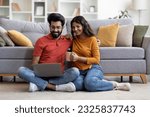 Small photo of Domestic Pastime. Happy Young Indian Spouses Resting With Laptop At Home, Smiling Eastern Couple Relaxing On Floor In Living Room, Browsing Internet And Drinking Coffee Together, Free Space