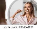 Small photo of Beautiful Mature Female Brushing Her Teeth With Toothbrush Near Mirror, Happy Middle Aged Woman Smiling At Her Reflection, Making Morning Hygiene At Home, Doing Oral Care Treatments, Selective Focus