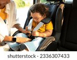 Asian Mom Sitting Down Her Toddler Daughter In Baby Car Seat, Adjusting Harness Straps For Safety During Automobile Journey. Cropped Shot, Closeup Of Child In Chair For Safe Auto Trip