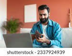 Small photo of Frustrated Indian man holding empty wallet without money, struggling with financial issues during crisis, posing sitting near computer at home, checking his bank balance. Finance issues