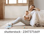 Tired infant baby cries in mother hands, depressed unhappy exhausted mom sitting on floor with crying little child on her lap, bedroom interior, copy space. Postnatal postpartum depression concept