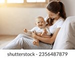 Young caucasian mom holding baby toddler, hugging carrying adorable little daughter, posing together at home, sun flare. Child care, motherhood and maternity leave concept. Empty space for text