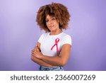 Breast Cancer Awareness. Black Young Woman With Pink Ribbon On T-Shirt Standing Over Purple Background In Studio, Crossing Hands Looking At Camera. Portrait Shot. Oncology Treatment