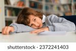 Small photo of Disengaged schoolboy lying on his desk in primary school classroom during seemingly boring lesson, moments of disinterest briefly capture the day