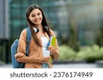 Small photo of Smiling student holding books, posing at college campus. Radiant pretty young woman holding books, standing at university, symbolizing a blend of joy and scholarly pursuits, copy space