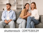 Relationship Vs Friendship. Woman Talking To Female Friend And Using Smartphone, Having Fun Ignoring Her Husband, While Man Sitting Bored Near Cheerful Girlfriends Indoor
