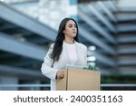 Small photo of Sad Hispanic business lady carrying cardboard box with her belongings, leaving office building after layoff, reflecting economic challenges of corporate dismissal and unemployment