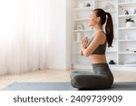 Small photo of Tranquil young asian woman meditating at home, practicing yoga with clasped arms, beautiful korean female sitting in prayer position on mat in living room, radiating inner peace, copy space