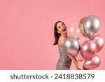 Small photo of Joyful caucasian woman in a glittering silver dress laughs heartily, clutching a bunch of shiny metallic and transparent balloons, enjoying a festive moment on a pink background