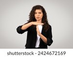 Small photo of Serious businesswoman in suit making timeout gesture, symbolizing the need for break or pause in corporate environment, standing on gray studio background