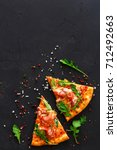 Small photo of Slices of pizza with prosciutto and rocket salad with spices on black background, copy space, top view