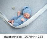 Newborn baby boy sleeping with knitted heart toy during studio photoshoot. Adorable infant child kid sleeping wearing hat and costume