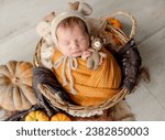 Small photo of Newborn baby girl swaddled in white fabric sleeping in basket decorated with pumpkins. Infant child kid napping on fur autumn studio portrait