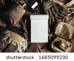 Photo of a blank notebook laying on military table with helmet, glasses, bullet shells, gloves and flask upper view.