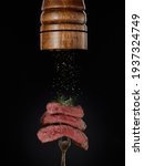 Small photo of Roasted meat. Milled spices falling from pepper mill on grilled pieces of beef steak medium rare on fork on black background. Steak menu. Grilled menu.