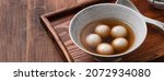 Small photo of Close up of sesame big tangyuan (tang yuan, glutinous rice dumpling balls) with sweet syrup soup in a bowl on wooden table background for Winter solstice festival food.