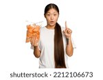 Small photo of Young asian woman holding crips isolated on green chroma background having some great idea, concept of creativity.