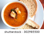 A bowl of fresh tomato soup in white ceramic bowl, garnished with herbs, croutons, seasoning and a drizzle of olive oil, and served with crusty wholemeal bread.