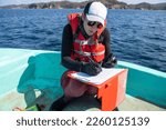 Equipped marine biologist writing notes on a paper while working on a boat