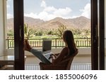 Young woman relaxing with a white modern laptop computer on a balcony, tropical view