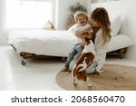 Small photo of Happy young mother and her 2 year old son sit on the floor in bedroom and play with dog, jack rassel puppet. Dog and happy family