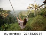Small photo of Rear view woman on a swing at vacation in Bali, Indonesia. Young girl traveler sitting on the swing in beautiful nature place in the mountains, tropical jungle view