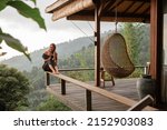 Young beautiful woman drinking coffee while sitting on a balcony in a wooden house overlooking the mountains