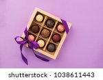 A set of assorted chocolates in a paper box with a satin purple ribbon on a bright background. A place for design. Flat layout. Celebratory concept. Copy space