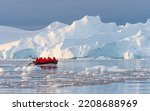 Small photo of Antarctic expedition, cruise passengers in red parkas ride in a Zodiac inflatable boat, very close to a huge white iceberg in Cierva Cove bay