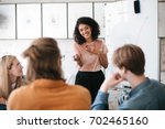 Beautiful African American lady with dark curly hair happily speaking about new project with her colleagues in office. Young smiling business woman giving presentation to coworkers