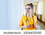 Joyful young nurse. Smiling young girl in yellow uniform, and looking at camera, in front of window clinic. The concept of health
