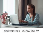 A young woman using a laptop communicates over the Internet with a client from the living room. Cozy workplace, remote work, e-learning concept