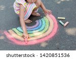   Kids paint outdoors. Portrait of a child girl drawing  a rainbow colored chalk on the asphalt on summer sunny day. Creative development of children