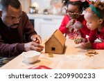 African American family decorating a gingerbread house together on Christmas day. Christmas moments with kids at home concept. Selective focus