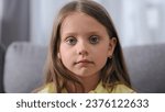 Small photo of Cute small kid look camera. One unhappy child sit sofa. Blue eyes gaze close up. Serious face portrait. Sad little girl cry. Brown hair model. Upset head shot. Young pretty person pose. Bad school day