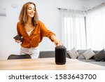 Small photo of Young woman turning on wireless smart column at home. Concept of a smart home wireless devices. Concept of smart home and voice command control