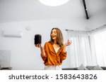 Small photo of Young cheerful woman controlling home devices with a voice commands, talking to a smart column at home. Concept of smart home and voice command control