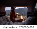 Woman photographing a bonfire on phone, traveling by car in the mountains at dusk. Camping and vacation in the mountains alone, travel by car concept