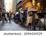 Small photo of Woman sitting on crowded street at bar or restaurant outdoors in Bologna city. Concept of Italian lifestyle and gastronomy