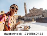 Woman having italian breakfast with coffee and croissant, sitting at outdoor cafe with beautiful view on main square of Siena city. Concept of italian lifestyle and travel old towns in Tuscany