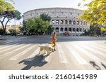 Woman crossing street with her dog in front of Coliseum in Rome. Street view with the most popular italian landmark
