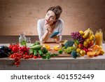 Young and pretty woman using smart phone sitting at the table full of fruits and vegetables in the wooden interior. Counting calories with mobile app. Food and health care concept