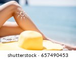 Woman sunbathing on the beach. Close-up view on the legs with lotion sun shape and yellow hat