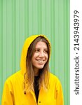 Small photo of Close-up side portrait of blonde woman wearing a raincoat. Horizontal view of caucasian woman in the street with yellow raincoat isolated on green wall. People isolated in background with copy space.