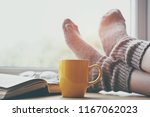 Woman resting keeping legs in warm socks on table with morning coffee and reading book