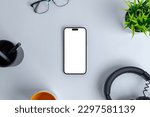 Modern work environment, with a blank phone screen islated for mockup, set among office essentials like a headset, plant, glasses, pens, and a coffee mug. Top view, flat lay composition