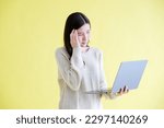 Small photo of Stress asian woman struggle with laptop computer, Frustrated asia female holding laptop computer while standing over yellow isolated background, People struggle with technology