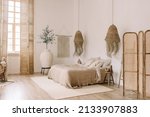 Small photo of Spacious, bright bedroom with white walls and a large bed in warm boho tones. Straw chandeliers, a large decorative vase, wooden shutters on the windows.